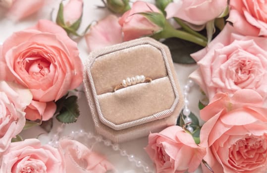 Engagement ring in a box between light pink roses and buds close up, romantic wedding preparations. Marriage proposal concept, valentines day scene
