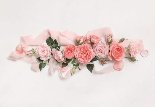 Romantic falt lay with light pink roses, petals and buds, green leaves and silk ribbons top view on white textured table . Mother's day or valentine's day concept, spring mood