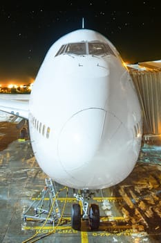 generic modern passenger aircraft at the gate by night ready for boarding without logos at the apron