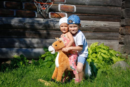 On a summer day, a girl and a boy swing on a toy horse with a white mane close-up on the street