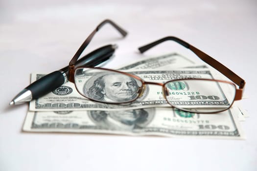 Glasses are lying on dollars with a black pen on a white table close-up