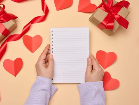 Open notebook with empty white sheets and gift boxes around on a yellow background, top view. Festive background for wish