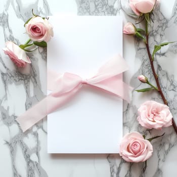 A flat lay composition of a soft pink wedding invitation with a delicate bow, accompanied by roses and set against a marbled background.