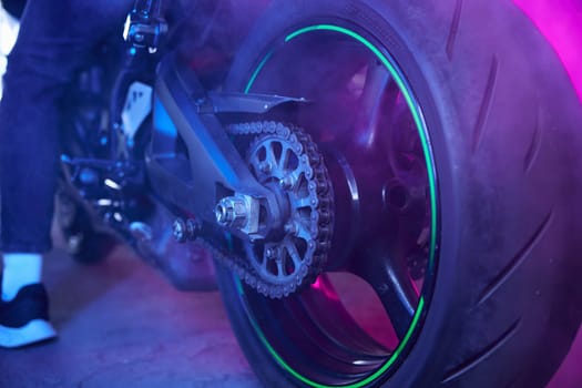 Sport motorcycle wheel view from back in neon light and smoke. Street racing training at driving school motordrome for practice