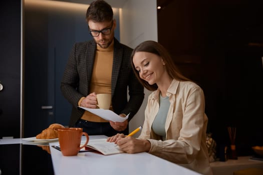 Serious husband holding paper asking wife about additional costs feeling dissatisfied, irritated and misunderstanding about female wastefulness. Family budget and economy