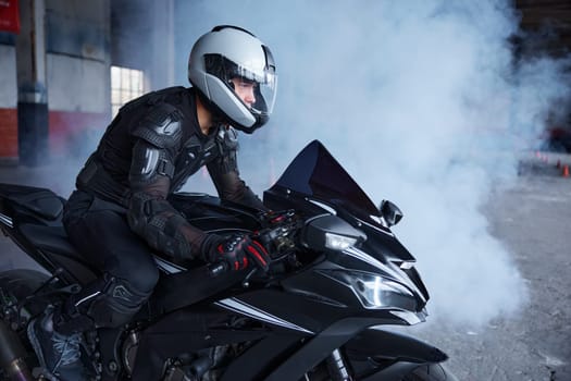 Biker wearing protective helmet and uniform for speed riding at training class of motordrome of professional driving school