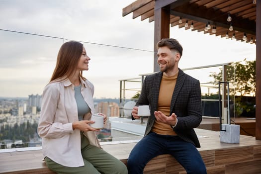 Man and woman coworkers having nice conversation sharing ideas emotionally speaking at balcony. Freelancers team taking coffee break during workday in office