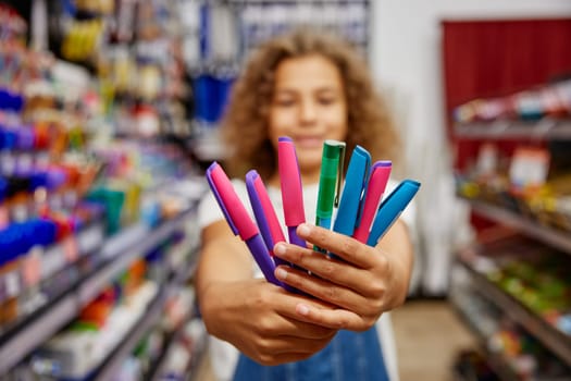 Selective focus school girl holding variety of pens for writing standing at stationery store. Creative tools for education concept
