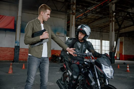 Personal lesson at motorcycle school. Male instructor teaching young biker explaining important things before start to move