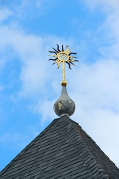 Sun-shaped outbuilding on tiled roof. Figurine on the roof of an old building