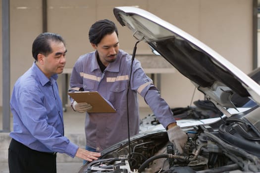 Two guys are standing by a car with the hood open, staring at the engine inside.
