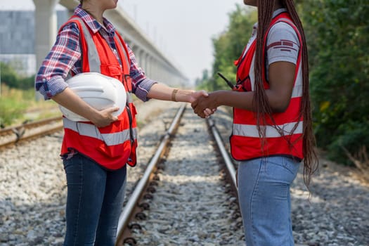 Two women wearing hard hats are shaking hands on some railroad tracks.