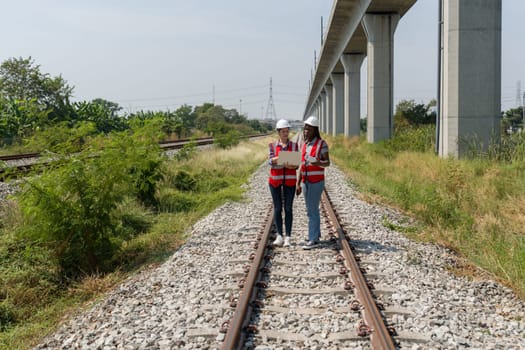 Two people are standing on railroad tracks and looking at laptop computer together.