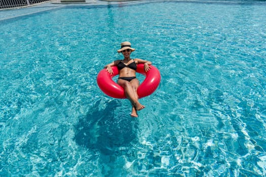 A lady enjoy a sunny day, floating on a bright inflatable ring in a clear blue swimming pool.