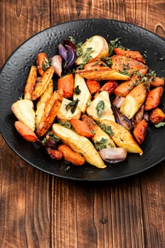 Healthy homemade roasted parsnip root, carrots and garlic on rustic wooden table.