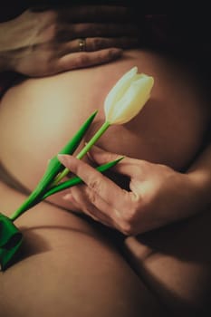 Pregnant woman expecting a baby, with a white tulip in her hand close-up