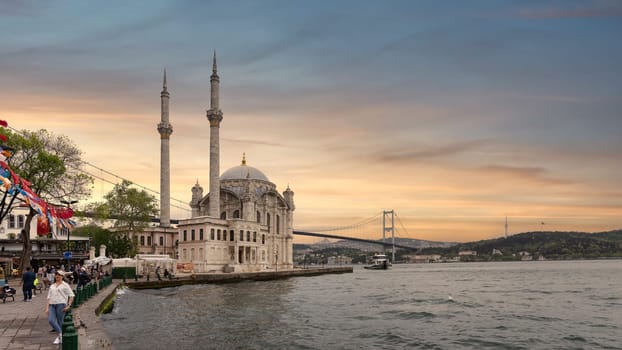 Istanbul, Turkey - May 12, 2023: A stunning view of Ortakoy Mosque sitting next to the Bosphorus Bridge with minarets and domes glistening in the rays at sunset in Ortakoy neihborhood