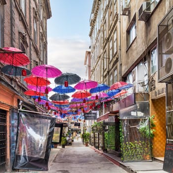 Istanbul, Turkey - May 13, 2023: Vibrant canopy of colorful umbrellas hangs suspended above an alley in Karakoy, in an eye catching installation that creates a whimsical and playful atmosphere