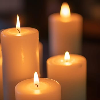 Close-up of lit white candles glowing warmly against a dark background