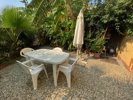 Cozy garden corner with white plastic furniture under an umbrella, surrounded by lush greenery for outdoor relaxation