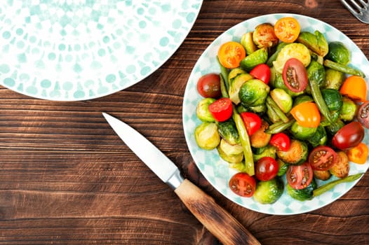 Salad of roasted brussels sprouts, tomatoes and green beans on a rustic wooden table. Flat lay with copy space.