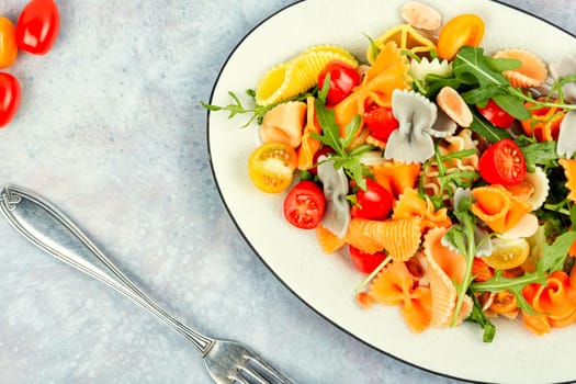 Salad with fresh tomatoes, greens and pasta on a plate.
