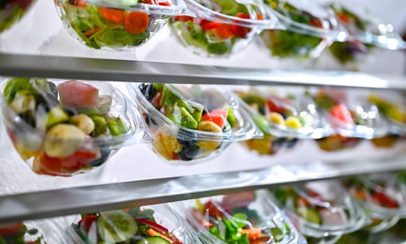 Plastic boxes with pre-packaged fruit and vegetable salads, put up for sale in a commercial refrigerator