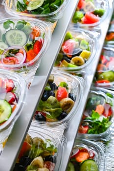 Plastic boxes with pre-packaged fruit and vegetable salads, put up for sale in a commercial refrigerator