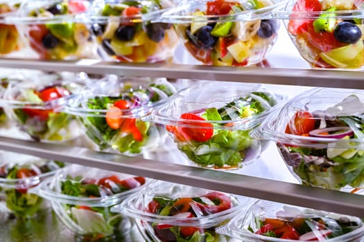 Plastic boxes with pre-packaged fruit and vegetable salads, put up for sale in a commercial refrigerator