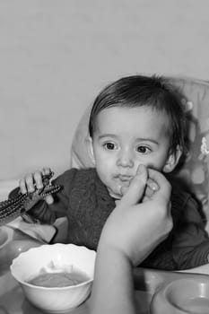 Feeding a small child with food while sitting at a children's table indoors in close-up.Monochrome photography