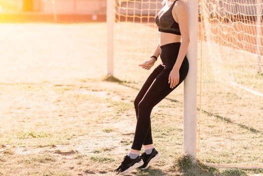 A female coach with dark hair stands on red running track of stadium, dressed in sports uniform.