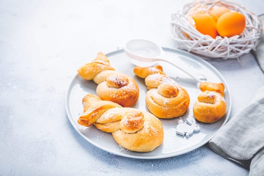 Buns made from yeast dough in a shape of Easter bunny and colored eggs