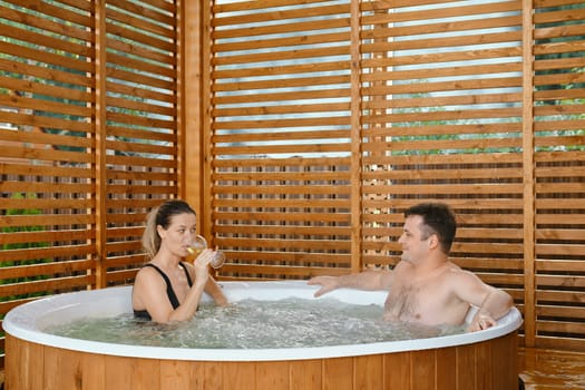 Beautiful couple in love relaxing and drinking wine in outdoor hot tub during weekend