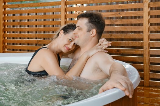 Lovely woman hugs her husband while spending time together in outdoor hot tub