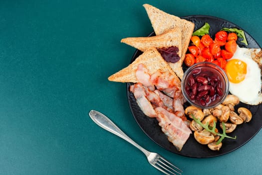 Fried bacon and eggs, toast and beans on rustic wooden table. Traditional English breakfast. Top view, flat lay.