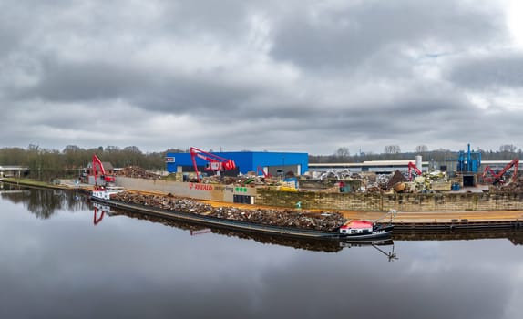 ALMELO, NETHERLANDS - FEBRUARY 17, 2024: scrap processing company along a canal with a ship full of metal scrap