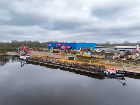 ALMELO, NETHERLANDS - FEBRUARY 17, 2024: scrap processing company along a canal with a ship full of metal scrap