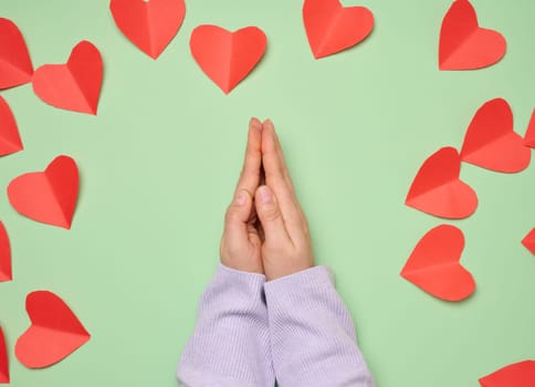 Woman's hands folded in a prayer pose on a green background with red hearts, top view