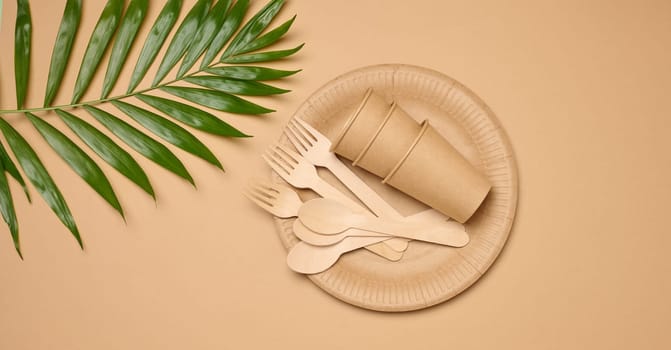 Paper plates and cups, wooden spoons and forks on a beige background, top view