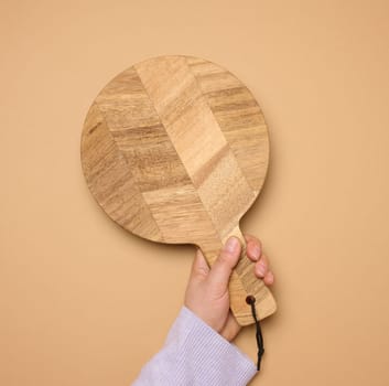 Woman's hand holding empty round wooden cutting board, top view