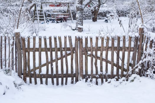 Snow-covered garden fence with garden gate at an allotment garden in winter, Germany