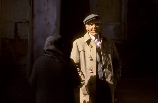 Lisbon, Portugal - July 4, 1992: portrait of old man in camelhair suit and backside of old lady in shadow.