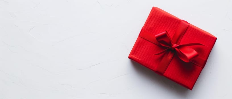 A vibrant red gift box with a satin ribbon lies on a textured white surface, evoking feelings of anticipation and celebration