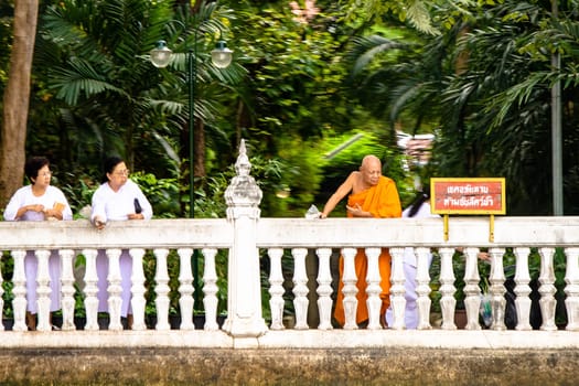 Bangkok, Thailand - December 26, 2007: women in white clothes and orange dressed monk throw blossons into the river to honor the godness