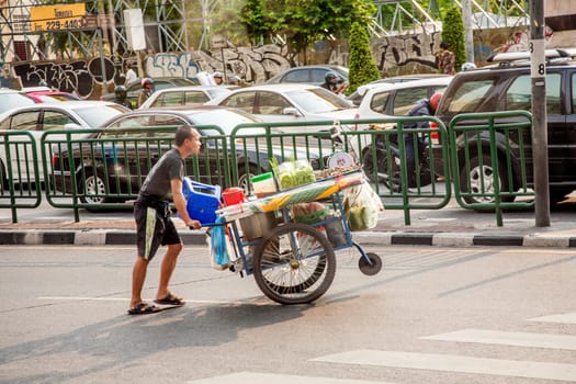 Bangkok, May 6, 2009: hawker with his rolling small kitchen offers noodle soup, vegetables and fresh fruit drinks to thze people at the street including car driver..