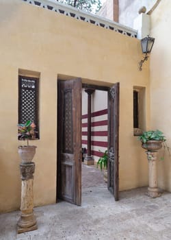 Open antique wooden decorated doorway mediating two wooden windows and leading to a peaceful courtyard with lush greenery and stone staircase