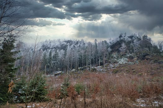 View of the great Zschirnstein with snow-covered trees and dramatic clouds with rays of sunshine, on the summit during a hike. From the nature park in the Elbe Sandstone Mountains. Landscape