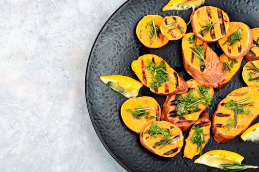Cut sweet potato baked with rosemary served on a black plate. Space for text.