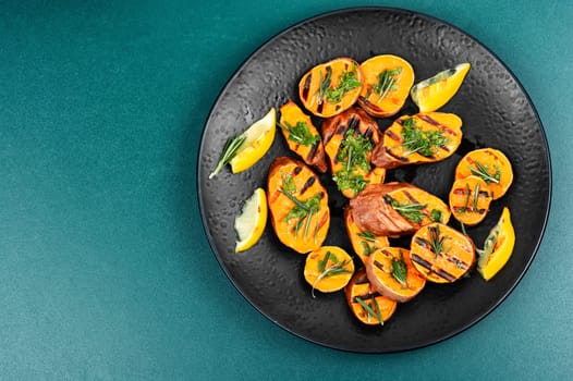 Cut sweet potato baked with rosemary served on a black plate. Space for text.