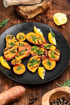Cut sweet potato baked with rosemary served on a black plate. Space for text.